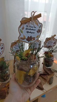 a person holding up a glass jar filled with plants and spices on top of a table