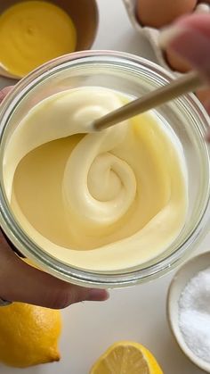 a person holding a spoon in a jar filled with mayonnaise and lemons