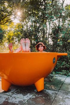 a woman is sitting in an orange bathtub with her feet up on the edge