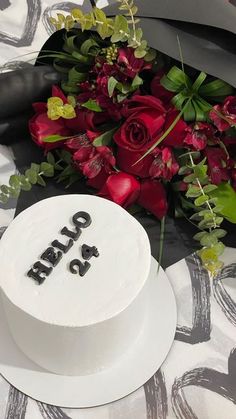 a white cake sitting on top of a table next to red roses and greenery