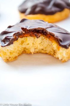 a half eaten chocolate covered doughnut sitting on top of a white table next to other pastries