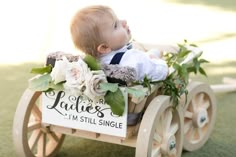 a baby sitting in a wooden wagon with flowers on the side and a teddy bear