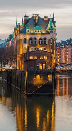 an old building is lit up at night on the water's edge with other buildings in the background