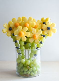 a vase filled with yellow flowers and green grapes