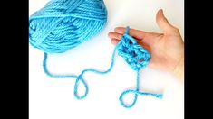 a hand holding a ball of blue yarn next to a crochet hook on a white surface