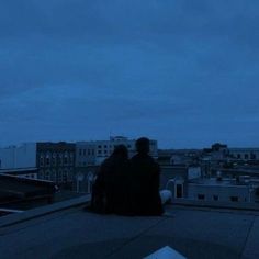 two people sitting on top of a roof at night