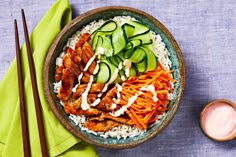 a bowl filled with rice, cucumbers and carrots next to chopsticks