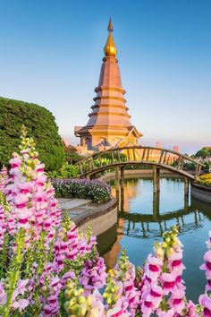 a bridge over a small pond with flowers in the foreground and a pagoda in the background