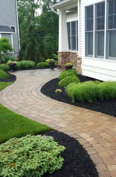 a brick walkway in front of a house with grass and bushes on the other side