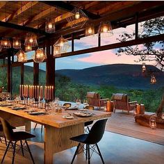 an outdoor dining area with wooden tables and chairs, overlooking the valley outside at dusk