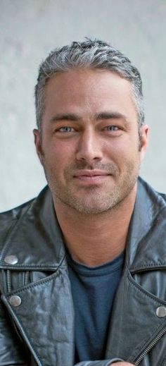 a man in a leather jacket is posing for a photo with his hand on his chest