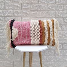 a pink and brown striped pillow sitting on top of a white table next to a brick wall