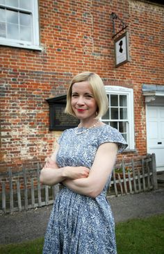 a woman standing in front of a brick building with her arms crossed and looking at the camera