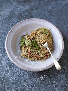 a white bowl filled with pasta and pesto on top of a table next to a fork