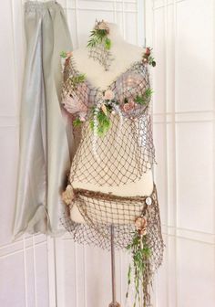 a mannequin is adorned with flowers and netting on display in front of a white wall