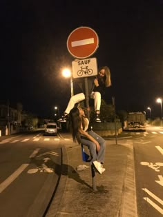 two women are sitting on a pole in the middle of the street and one is leaning over