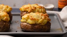 three baked potatoes on a baking sheet with cheese