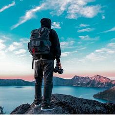 a man standing on top of a mountain looking at the water and mountains in the distance