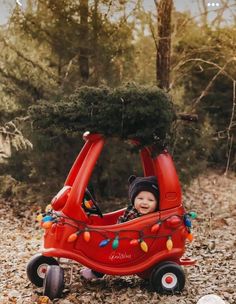 a small child in a red car with christmas lights on it's roof and trees growing out of the top