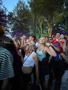 a group of people standing around each other at a music festival with trees in the background