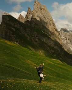 two people are flying a kite on a grassy field in front of some mountain peaks