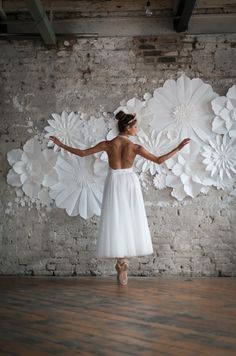 a woman in a white dress standing next to large paper flowers