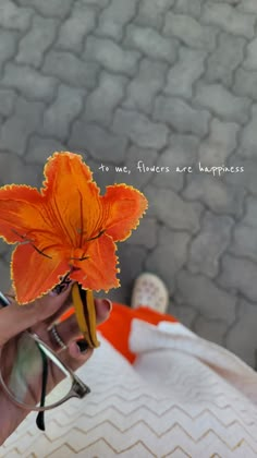 a person holding an orange flower in their left hand and reading glasses on the other