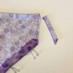 a piece of purple material with pins sticking out of it next to some thread and scissors