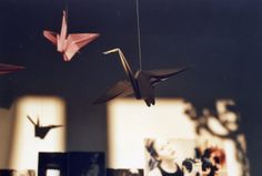 two origami birds hanging from strings in front of some pictures on the wall