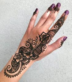 a woman's hand with henna tattoos on her left hand and purple nail polish