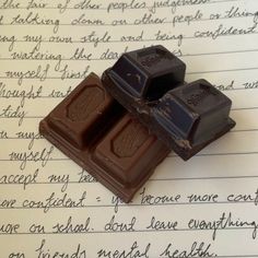 two pieces of chocolate sitting on top of a piece of paper with writing in the background