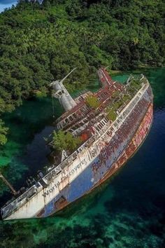 an old ship in the water with trees around it and blue water below that is surrounded by land