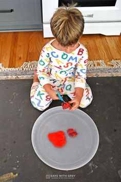 a little boy sitting on the floor playing with some red paint and scissors in front of an oven