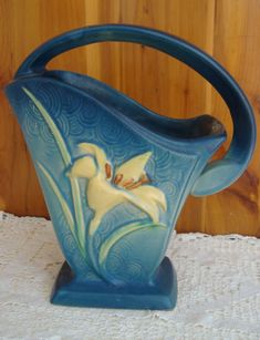 a blue vase sitting on top of a table next to a wooden wall and white lace