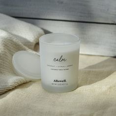 a candle sitting on top of a bed next to a white blanket and a cup