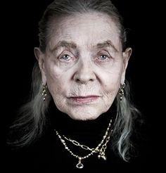 an old woman with grey hair and wearing gold necklaces on her neck is looking at the camera