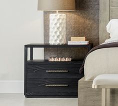 a night stand with two books on it next to a nightstand and lamp in a bedroom