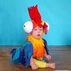 a baby sitting on the floor wearing a colorful bird costume and matching headdress