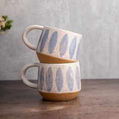 two coffee mugs sitting on top of a wooden table next to a flower vase