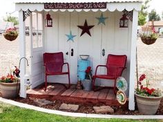 two red chairs sitting in front of a white shed with stars on the roof and windows