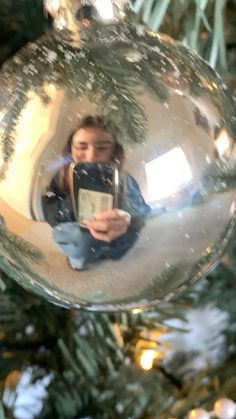 a woman taking a selfie in a glass ornament on a christmas tree