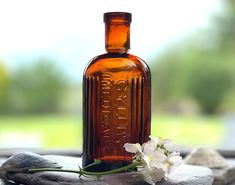 there is a small bottle with flowers in it sitting on the rocks next to some rocks