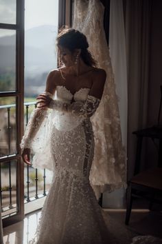 a woman standing in front of a window wearing a wedding dress