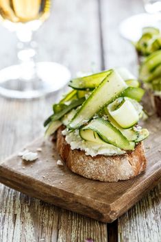 an open face sandwich with cucumbers and cheese on a cutting board next to a glass of wine