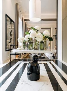 vases filled with white flowers sit on top of a marble table in the middle of a hallway