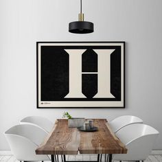 a dining room table with white chairs and a framed letter h on the wall above it