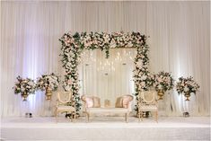 a decorated stage with chairs and flowers on the back drop cloths for an elegant wedding ceremony