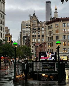 people are walking in the rain on a city street with tall buildings and green lights