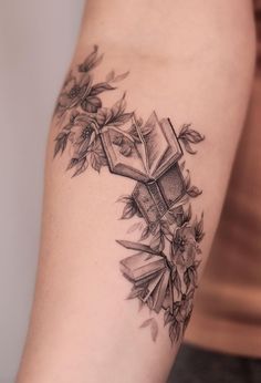 a woman with a tattoo on her arm has an open book and flowers around it