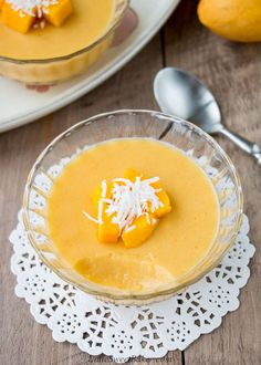 a bowl of mango custard with coconut on top and two spoons next to it